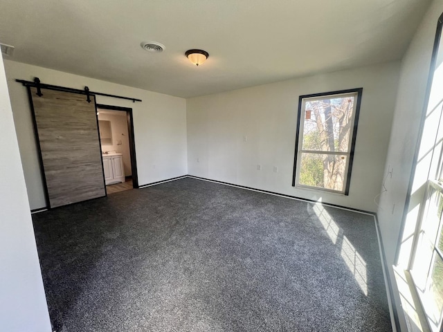 unfurnished bedroom with dark carpet, visible vents, and a barn door