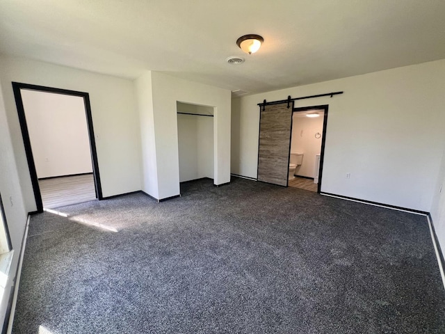 unfurnished bedroom with dark carpet, a closet, visible vents, a barn door, and baseboards