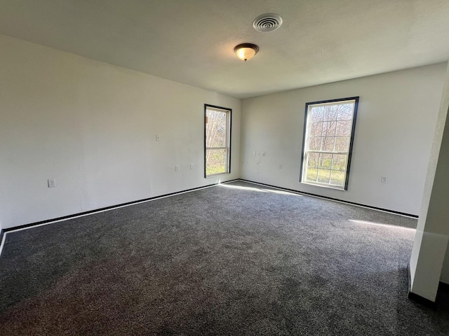 carpeted empty room featuring baseboards, visible vents, and a wealth of natural light