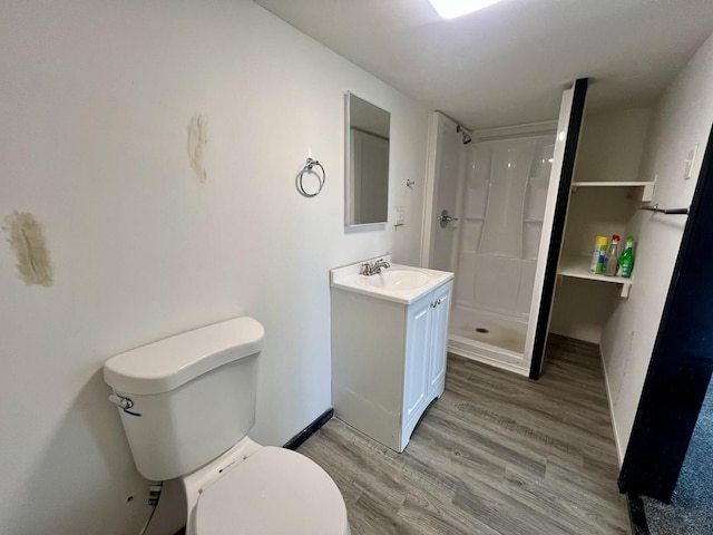 bathroom with baseboards, toilet, vanity, wood finished floors, and a stall shower