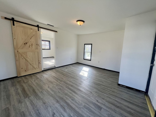 empty room featuring baseboards, plenty of natural light, a barn door, and wood finished floors