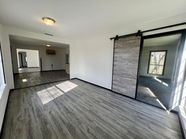 unfurnished room with wood finished floors, baseboards, and a barn door