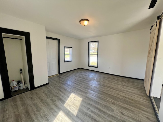 unfurnished bedroom featuring baseboards, a barn door, and wood finished floors
