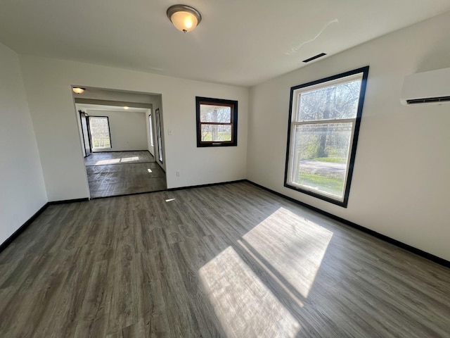 spare room with a wall unit AC, wood finished floors, and baseboards