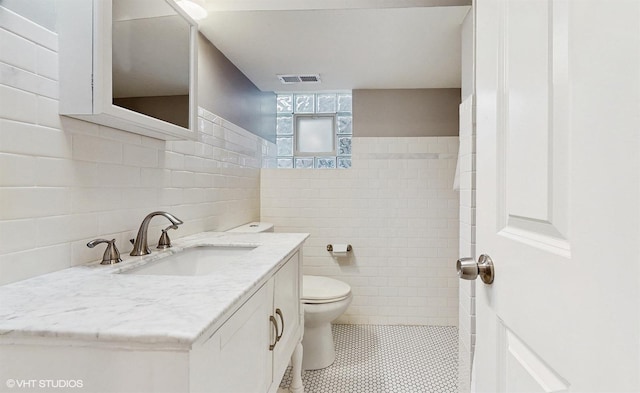 bathroom with visible vents, toilet, vanity, tile patterned floors, and tile walls