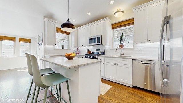 kitchen with a kitchen island, a breakfast bar, appliances with stainless steel finishes, white cabinets, and a sink