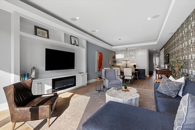 living room with baseboards, light wood finished floors, a raised ceiling, and recessed lighting