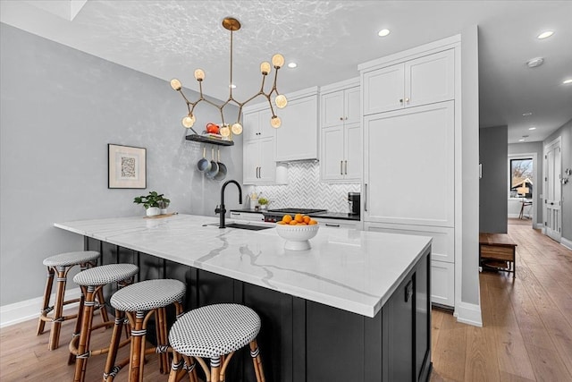 kitchen featuring a sink, white cabinetry, light wood-style floors, light stone countertops, and tasteful backsplash