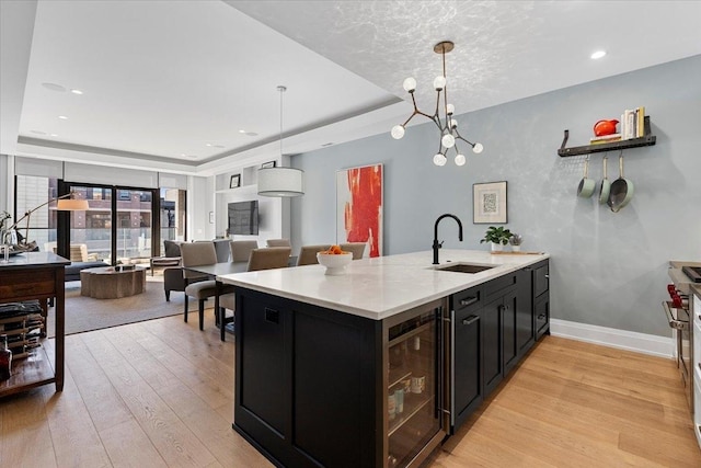 kitchen with a raised ceiling, light wood-style floors, a sink, dark cabinets, and beverage cooler