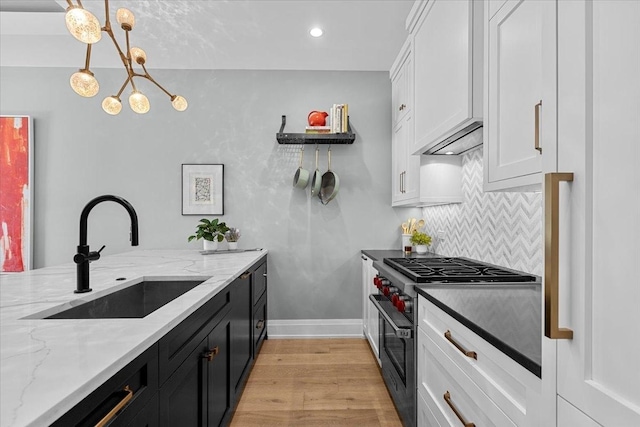 kitchen featuring light wood-style flooring, high end stainless steel range, a sink, dark cabinetry, and backsplash