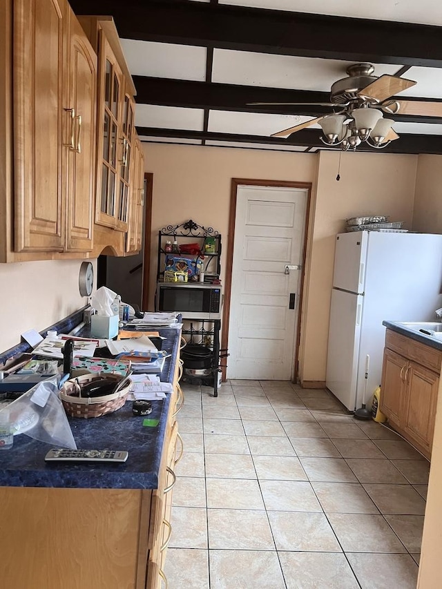 kitchen featuring light tile patterned floors, a ceiling fan, dark countertops, freestanding refrigerator, and beam ceiling