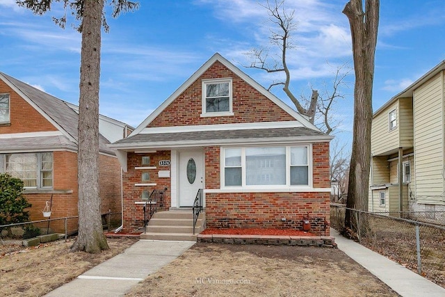 bungalow-style house with brick siding, fence, and roof with shingles