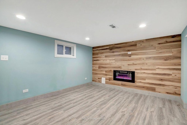 unfurnished living room featuring wood finished floors, wood walls, a glass covered fireplace, and recessed lighting