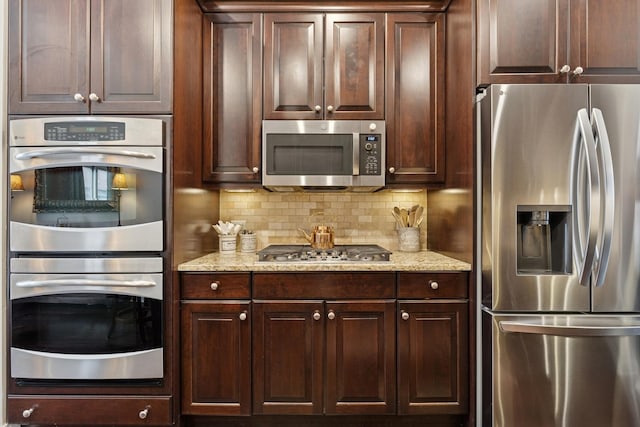 kitchen featuring dark brown cabinetry, backsplash, stainless steel appliances, and light stone counters