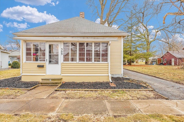 view of front facade with entry steps, a shingled roof, a chimney, and a front yard