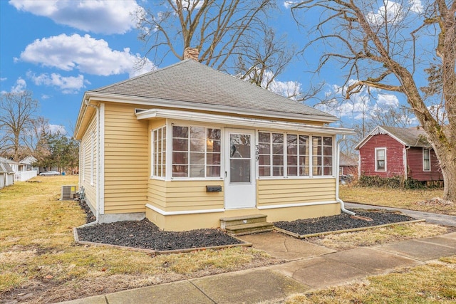 view of front of house with entry steps, a shingled roof, a sunroom, a front lawn, and a chimney