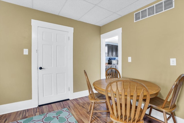 dining room featuring a paneled ceiling, wood finished floors, visible vents, and baseboards