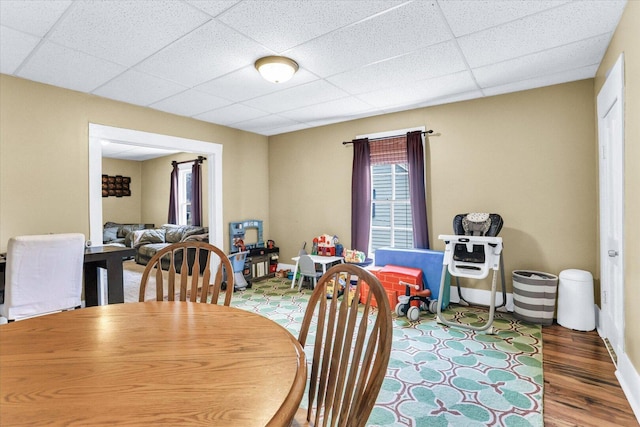 dining room featuring a drop ceiling, wood finished floors, and baseboards