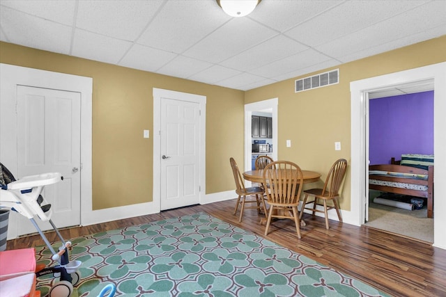 dining space with a paneled ceiling, baseboards, visible vents, and wood finished floors