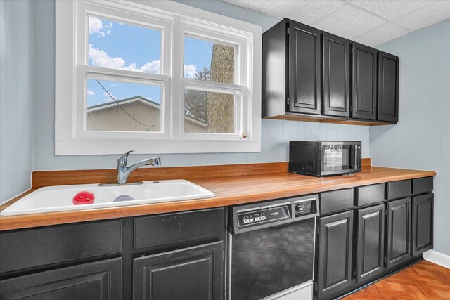 kitchen with dishwasher, dark cabinetry, a sink, and butcher block counters