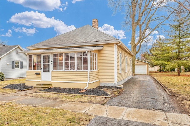 view of front facade featuring a garage, entry steps, a sunroom, a chimney, and an outdoor structure