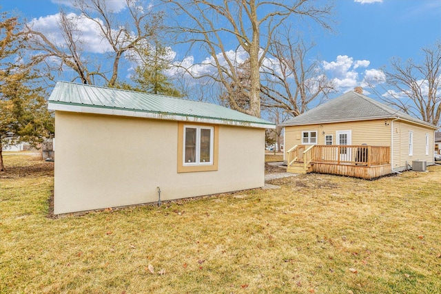 back of property with a deck, metal roof, central AC, an outdoor structure, and a yard