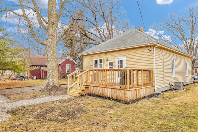 back of house with a chimney, a shingled roof, a lawn, central AC unit, and a wooden deck