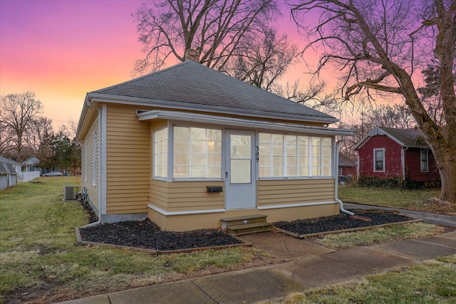 view of front of property with entry steps, a sunroom, roof with shingles, and a yard