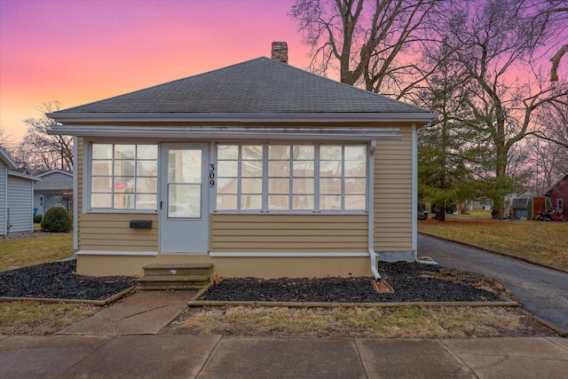 view of front of home with entry steps, a shingled roof, and a chimney