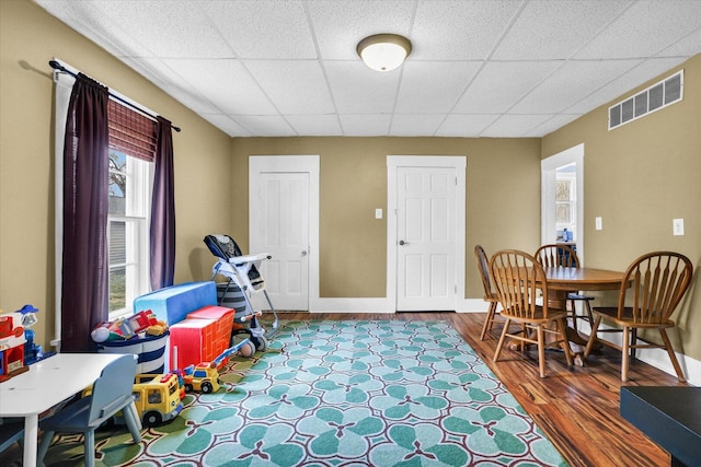 rec room with a paneled ceiling, visible vents, baseboards, and wood finished floors