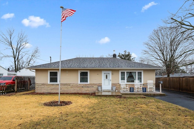 ranch-style house with stone siding, roof with shingles, a front yard, and fence