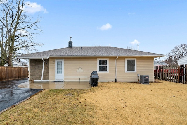 rear view of property with a fenced backyard, central AC, a lawn, roof with shingles, and a patio area