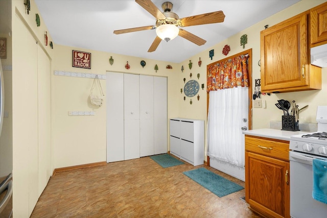 kitchen featuring under cabinet range hood, a ceiling fan, light countertops, white gas range oven, and brown cabinets