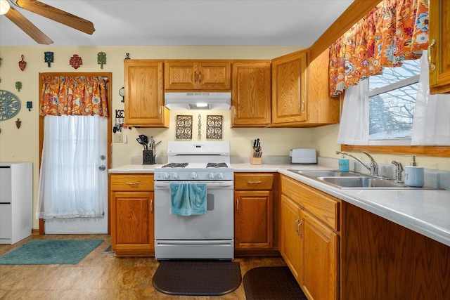 kitchen with light countertops, white gas stove, under cabinet range hood, and a sink