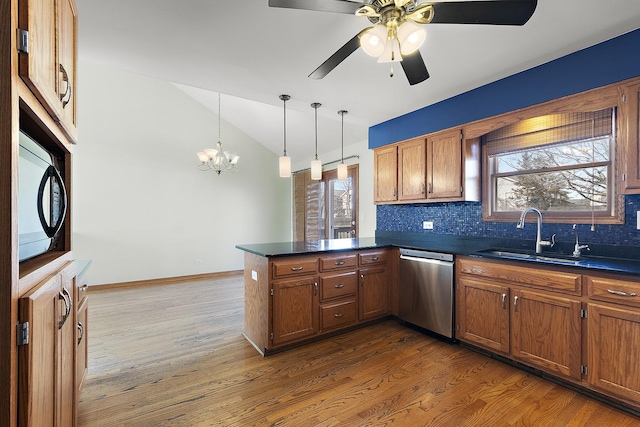 kitchen with a peninsula, lofted ceiling, a sink, stainless steel dishwasher, and dark countertops