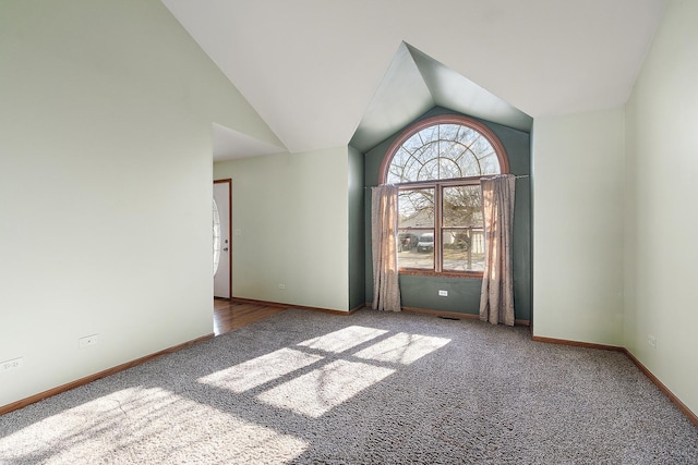 carpeted spare room featuring lofted ceiling and baseboards