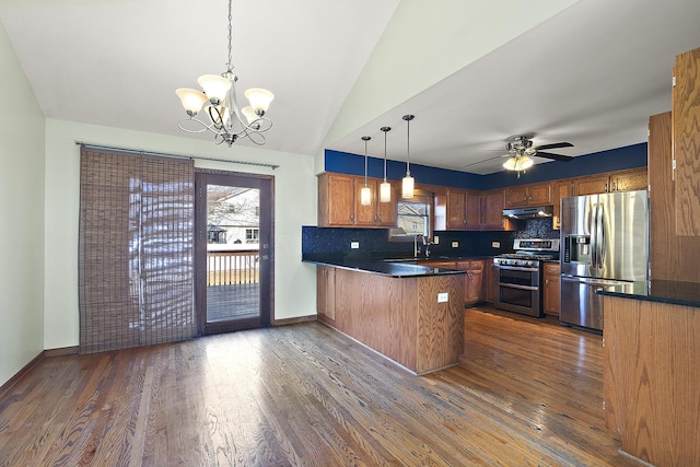 kitchen with under cabinet range hood, dark countertops, stainless steel appliances, a peninsula, and dark wood-style flooring