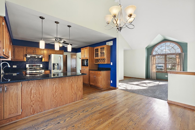 kitchen featuring backsplash, under cabinet range hood, ceiling fan with notable chandelier, appliances with stainless steel finishes, and a peninsula