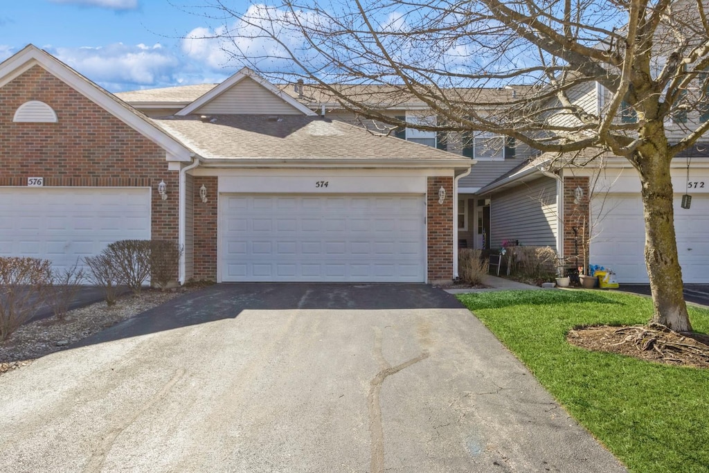 multi unit property featuring aphalt driveway, brick siding, an attached garage, and a shingled roof
