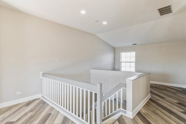 corridor with wood finished floors, an upstairs landing, visible vents, and baseboards