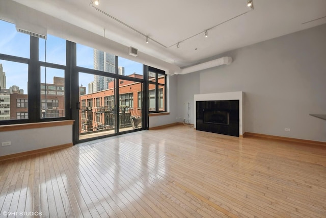 unfurnished living room with baseboards, hardwood / wood-style floors, rail lighting, a city view, and a fireplace