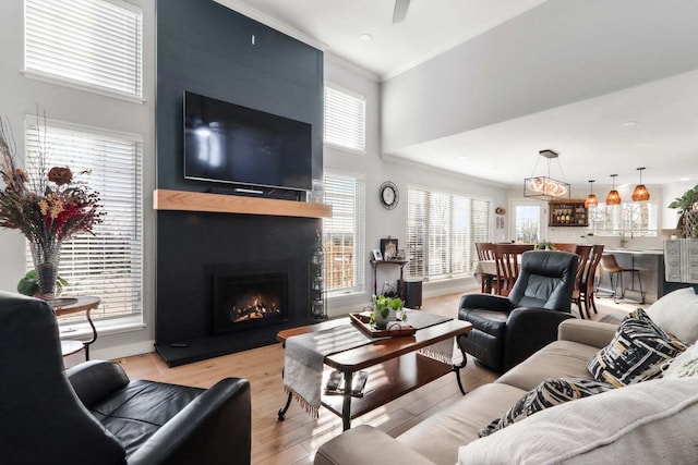 living room with light wood-style floors, a large fireplace, plenty of natural light, and ornamental molding