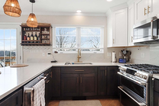 kitchen with ornamental molding, stainless steel appliances, light countertops, white cabinetry, and a sink