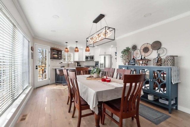 dining room featuring ornamental molding, baseboards, visible vents, and light wood finished floors