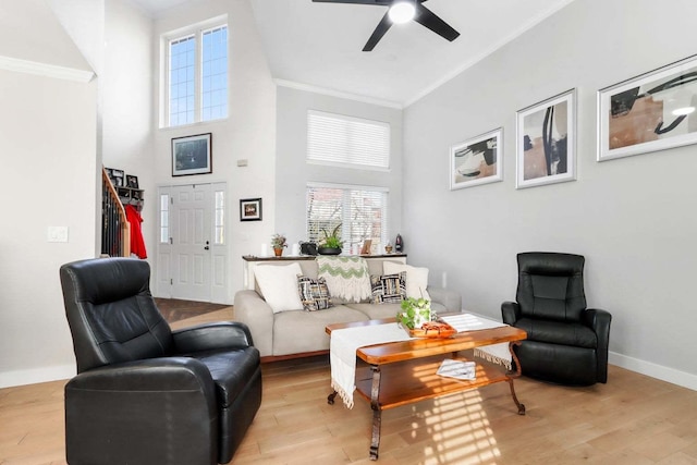 living area featuring a high ceiling, a ceiling fan, baseboards, light wood-type flooring, and crown molding