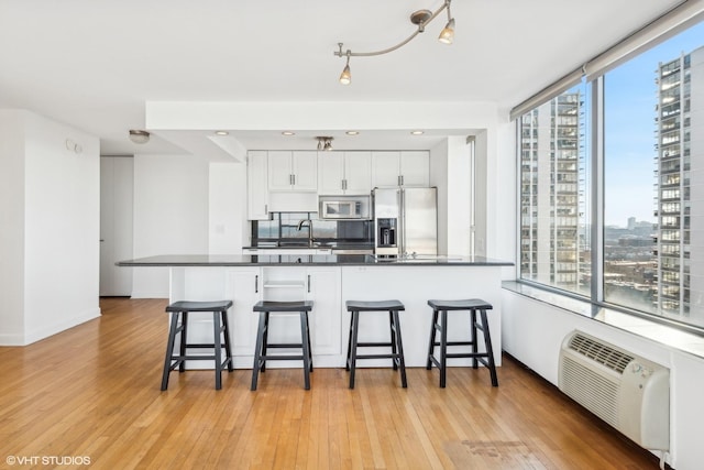 kitchen featuring light wood finished floors, dark countertops, appliances with stainless steel finishes, a kitchen bar, and a wealth of natural light