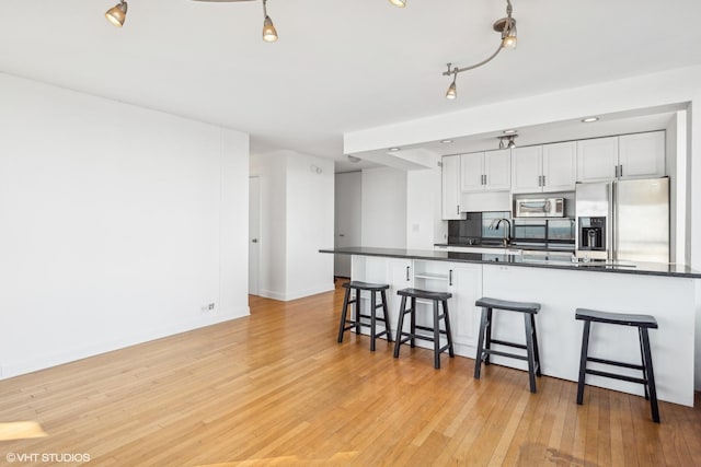 kitchen featuring dark countertops, light wood-style flooring, stainless steel appliances, a kitchen bar, and white cabinetry