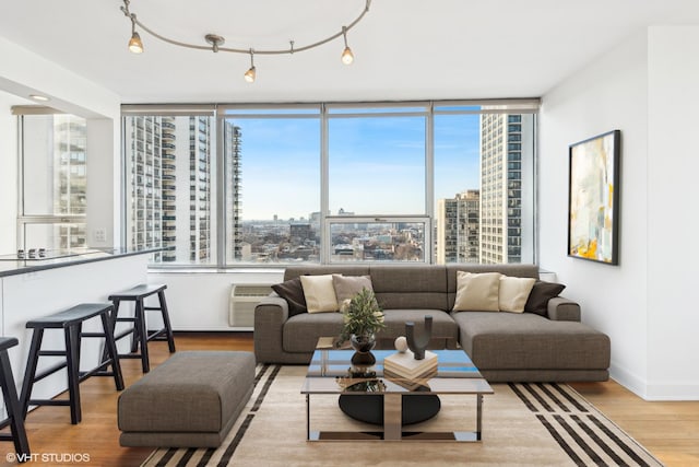 living room with baseboards, wood finished floors, a wall mounted air conditioner, rail lighting, and a view of city