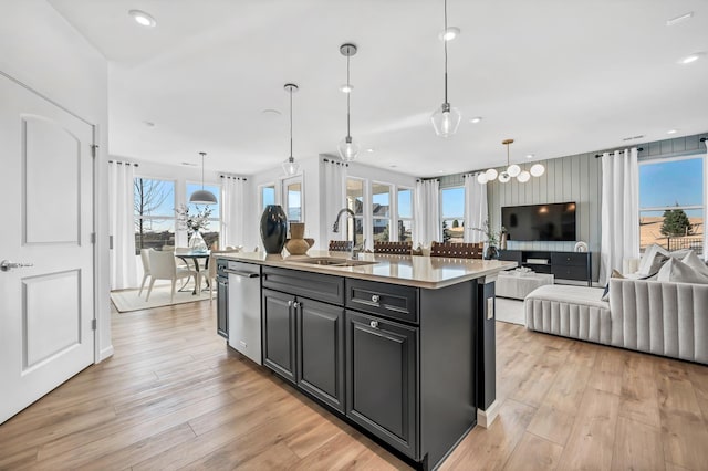 kitchen featuring an island with sink, open floor plan, light countertops, light wood-type flooring, and a sink