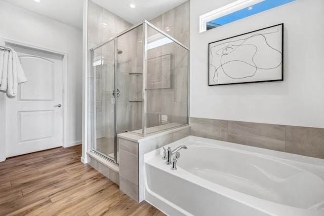 bathroom with a stall shower, a bath, and wood finished floors